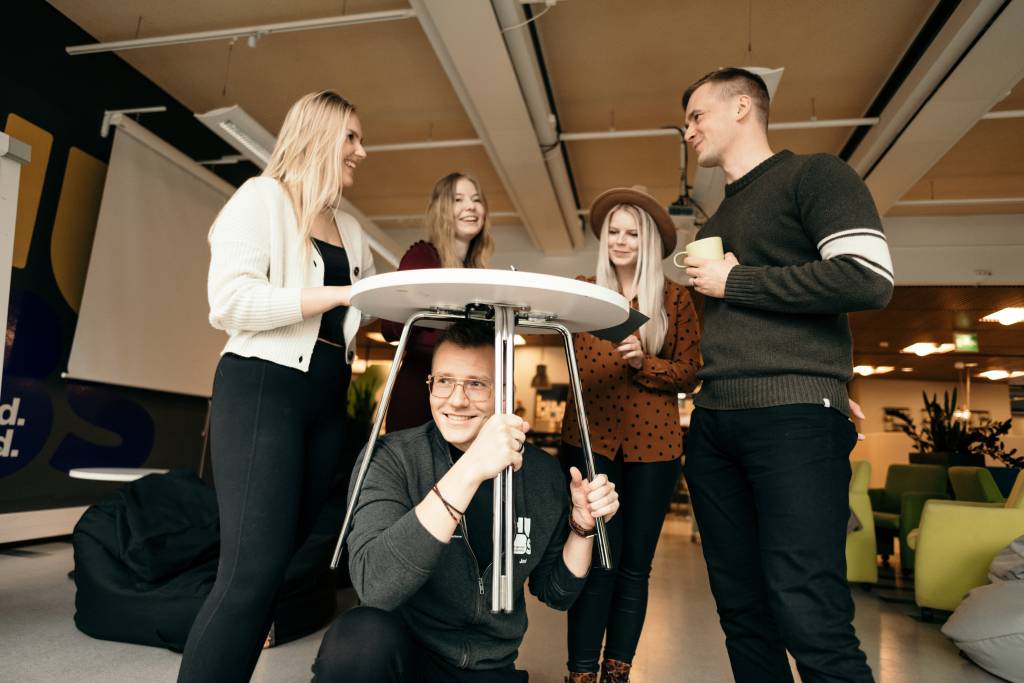 Valokuvassa tiimi kokoontuneena hauskasti pöydän ympärillä.