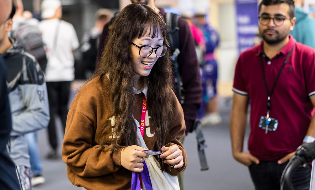 Students in the foyer of the University. In the foreground, a woman with dark hair is smiling and holding a batch intended for her overalls.