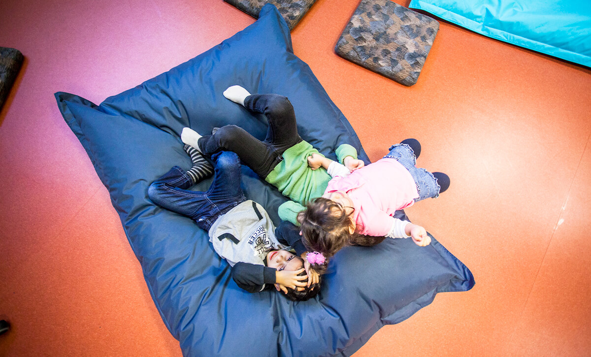 Three children are lying on a big blue pillow.
