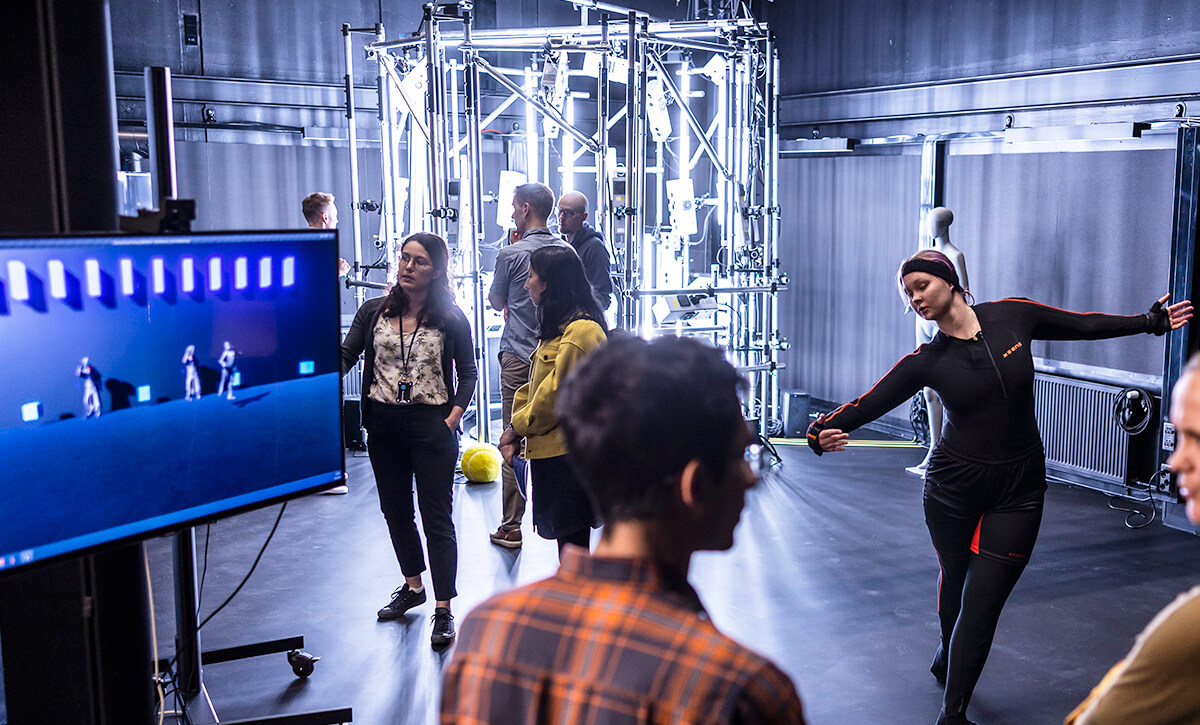 A dark space where a woman is dancing, and her movements are repeated on the screen. Students and staff are following the events.