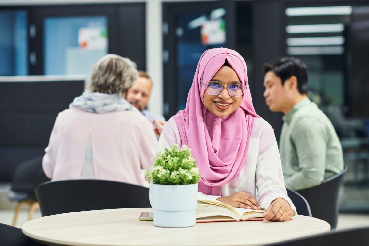 A young girl wearing a pink scarf smiling in a cafe room.