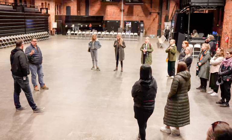 Ryhmä opiskelijoita kuuntelee opettajan puhetta