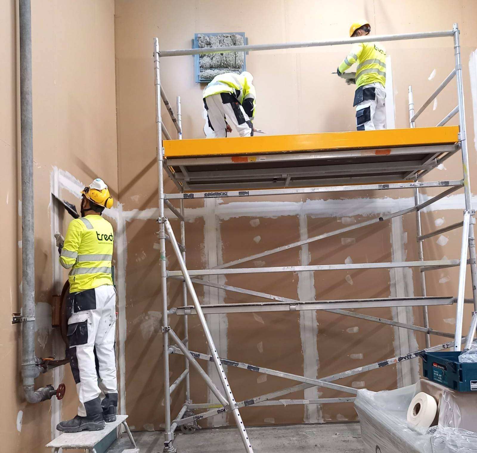 Tredun työvaatteisiin pukeutuneet remontoijat tasoittavat seinää.
