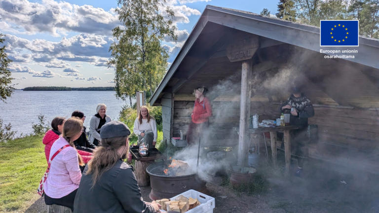 Ihmisiä nuotiolla laavun edessä. Taustalla järvi.