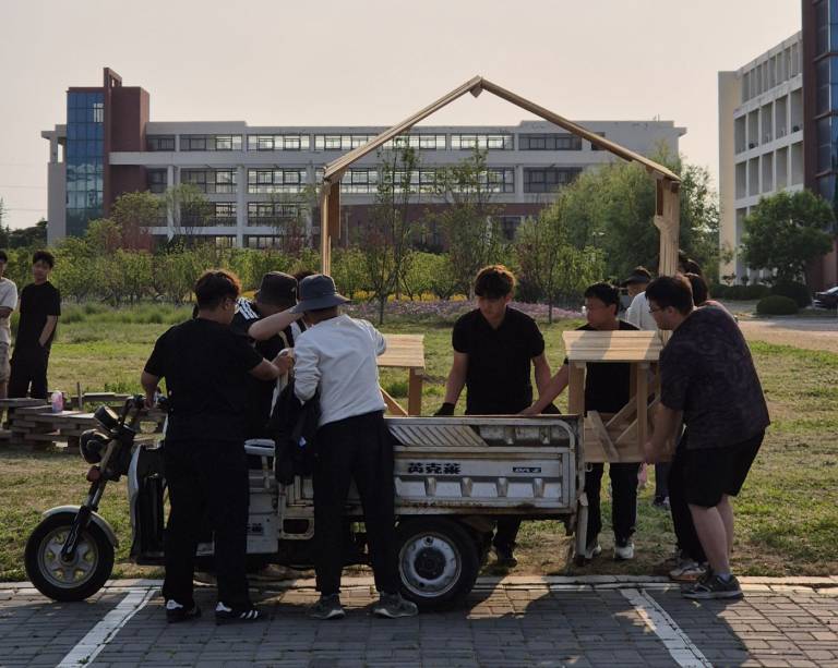 Opiskelijat kuljettavat paviljongin osaa puutyöverstaalta rakennuspaikalle.