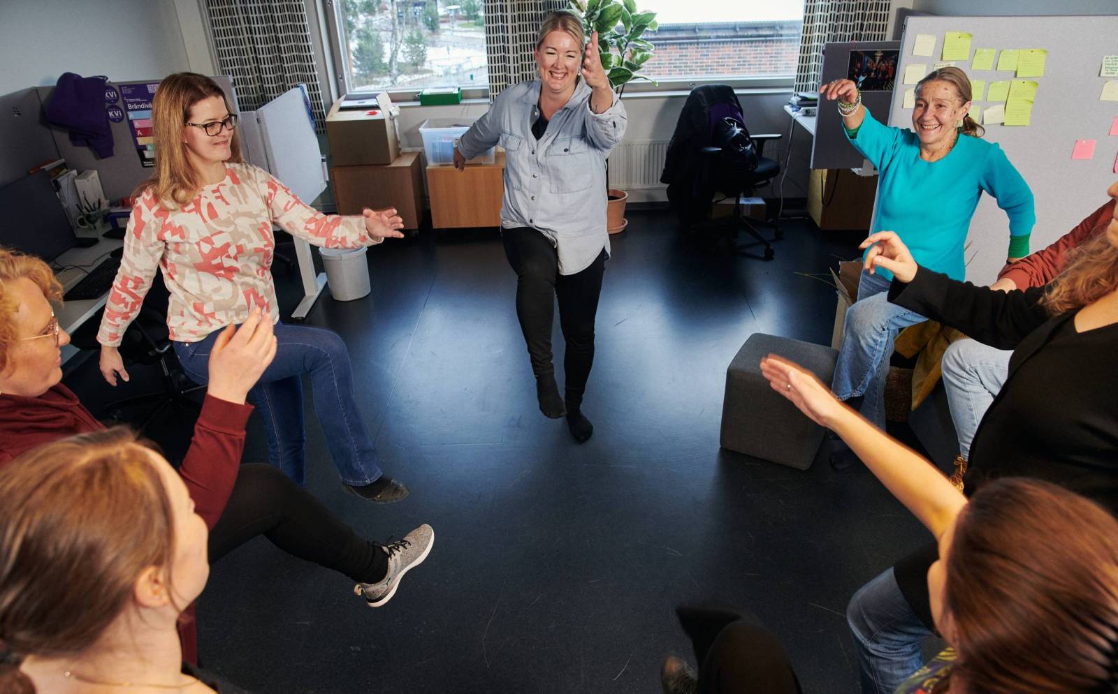 Ihmiset jumppaavat jalkoja nostellen ringissä hymyssä suin.