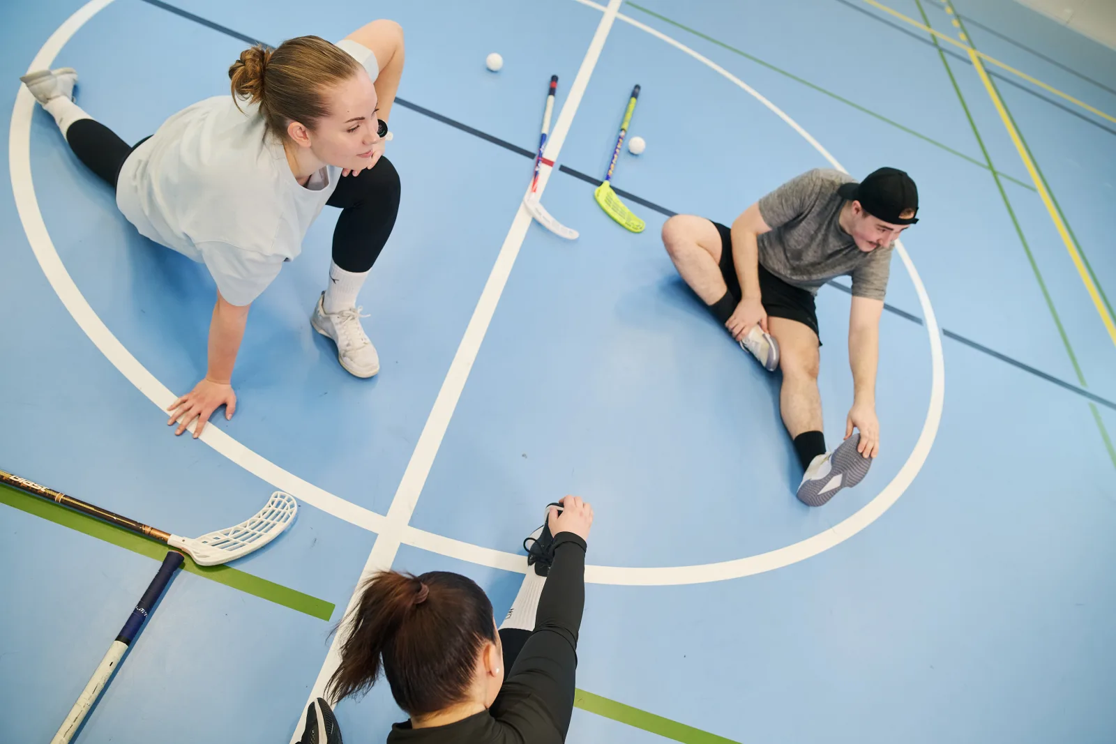 Three student in sports hall stretching.