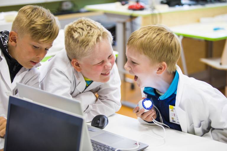Valokuva, jossa kolme iloista lasta työskentelemässä yhdessä mikroskoopilla.