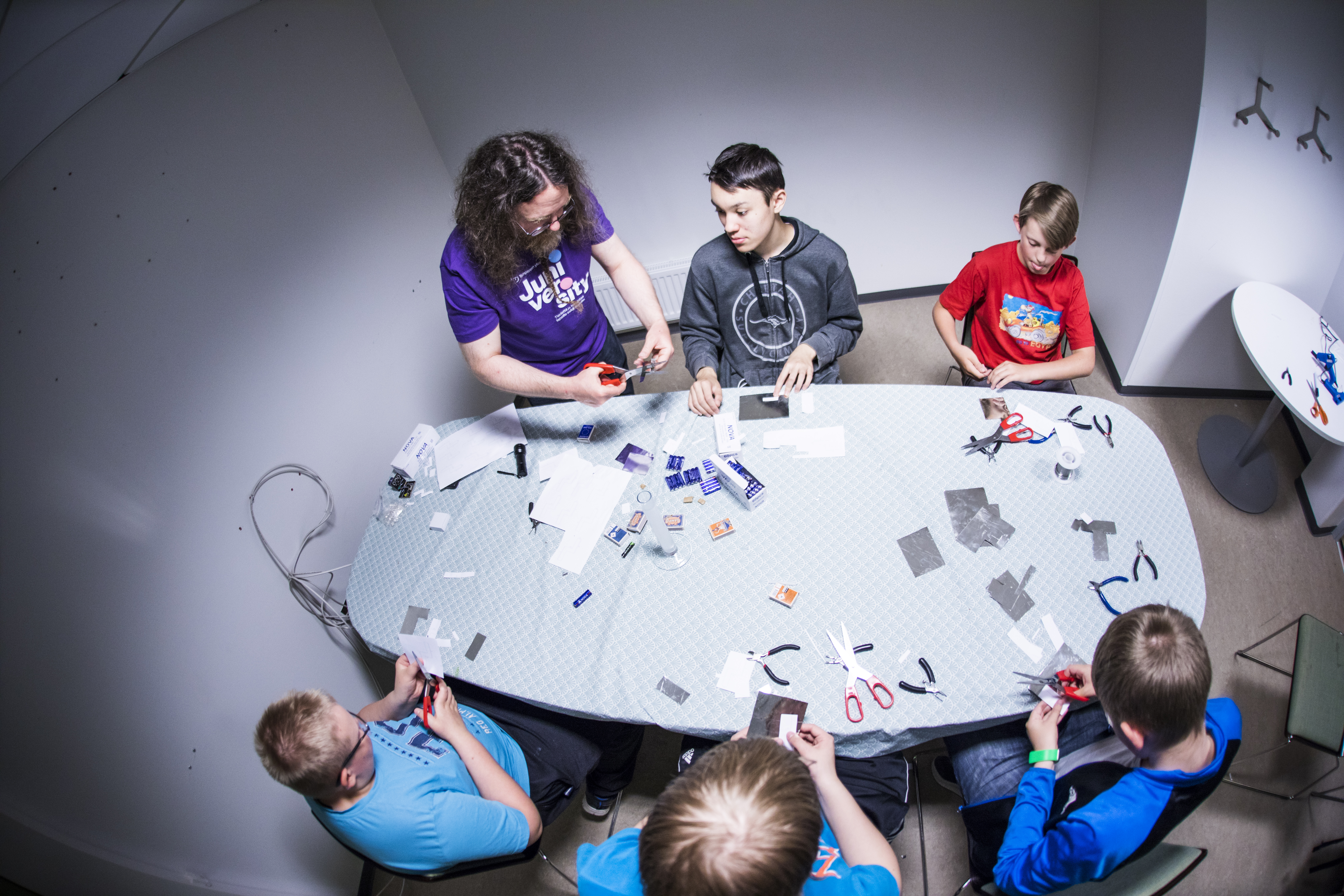 Valokuva, jossa juniversityn ohjaaja ja viisi nuorta työskentelemässä yhdessä elektroniikkaprojektin parissa.