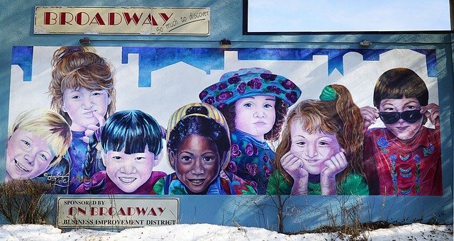 Muraali, jossa lapsia eri kansallisuuksista. Ylä- ja alapuolella Broadway-kyltit.