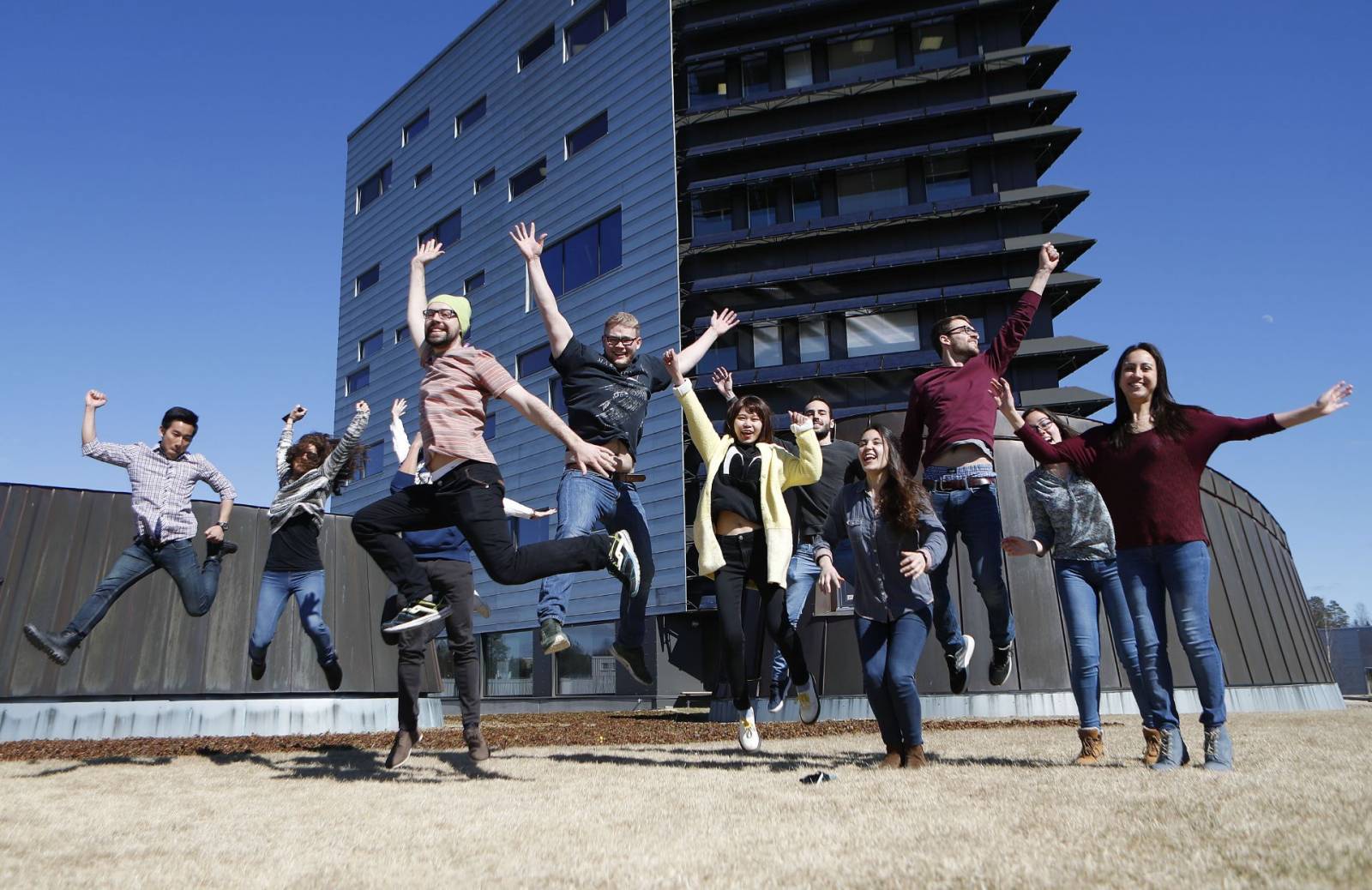 Valokuva, ryhmä nuoria hyppäämässä innokkaina ilmaan Tampereen yliopiston Hervannan kampuksen pihassa.