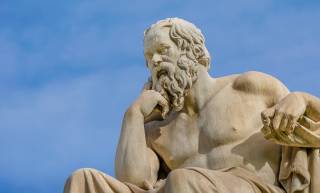 Kreikkalaisen Sokrates-filosofin vaalea patsas taivaansinistä taustaa vasten.