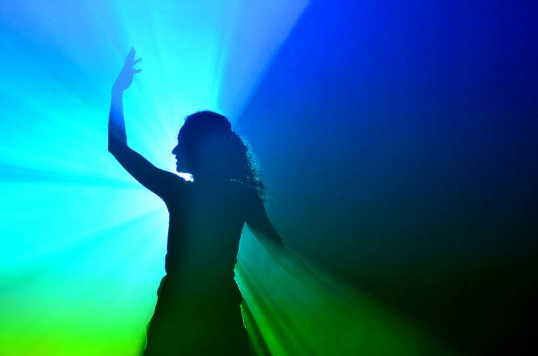 Nainen tanssii voimakkaan värillisen spottivalon edessä muodostaen silhuetin