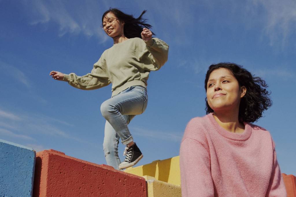 Two young women smiling, and one of them is jumping on colorful blocks.