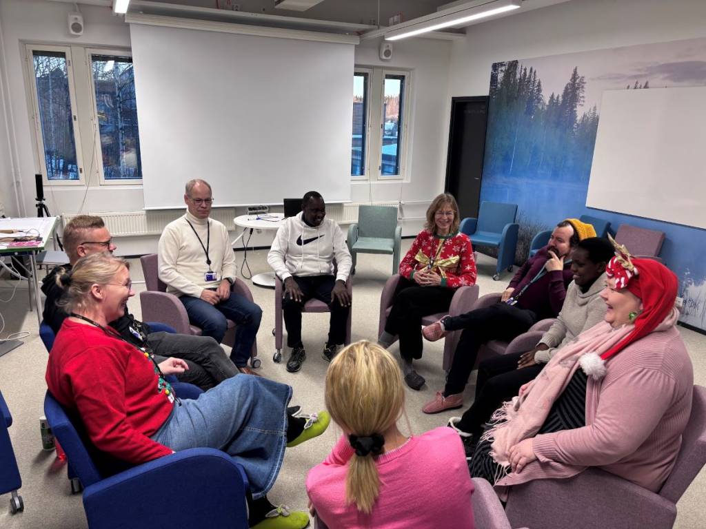 Nine persons sitting in a circle in a class room. 