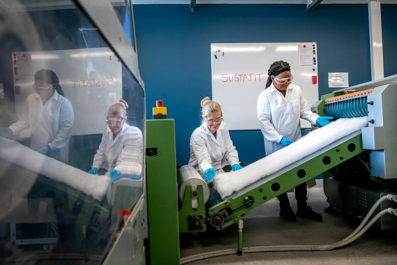 Two persons, a carded nonwoven batt on a conveyor belt of the needling machine.